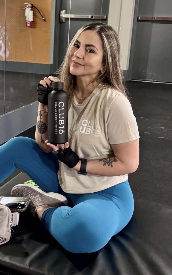 Carla, a Club16 Maple Ridge member of 11 years, sitting on a gym bench holding a Club16 water bottle